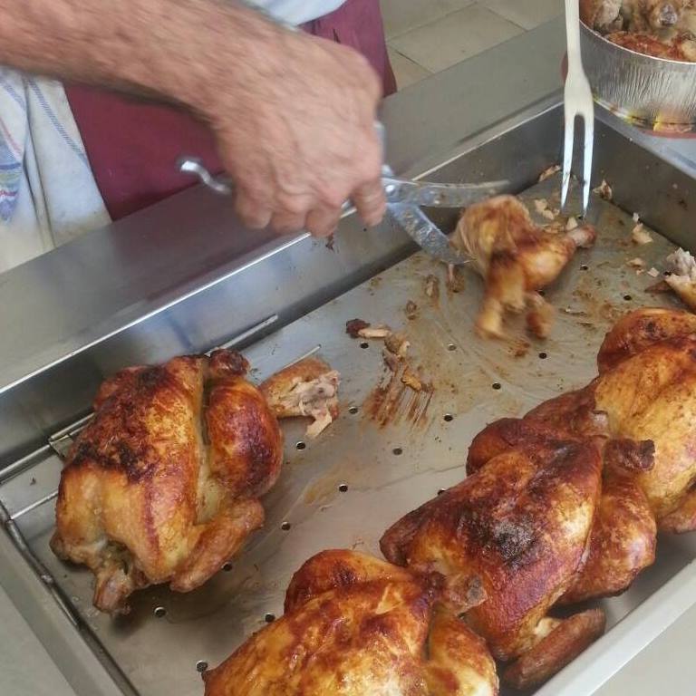 Una persona cortando pollo asado en una bandeja de metal.