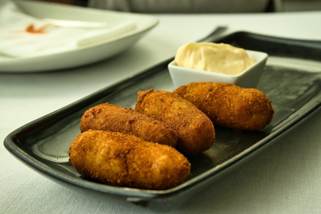 Croquetas empanizadas acompañadas de salsa alioli en una bandeja.